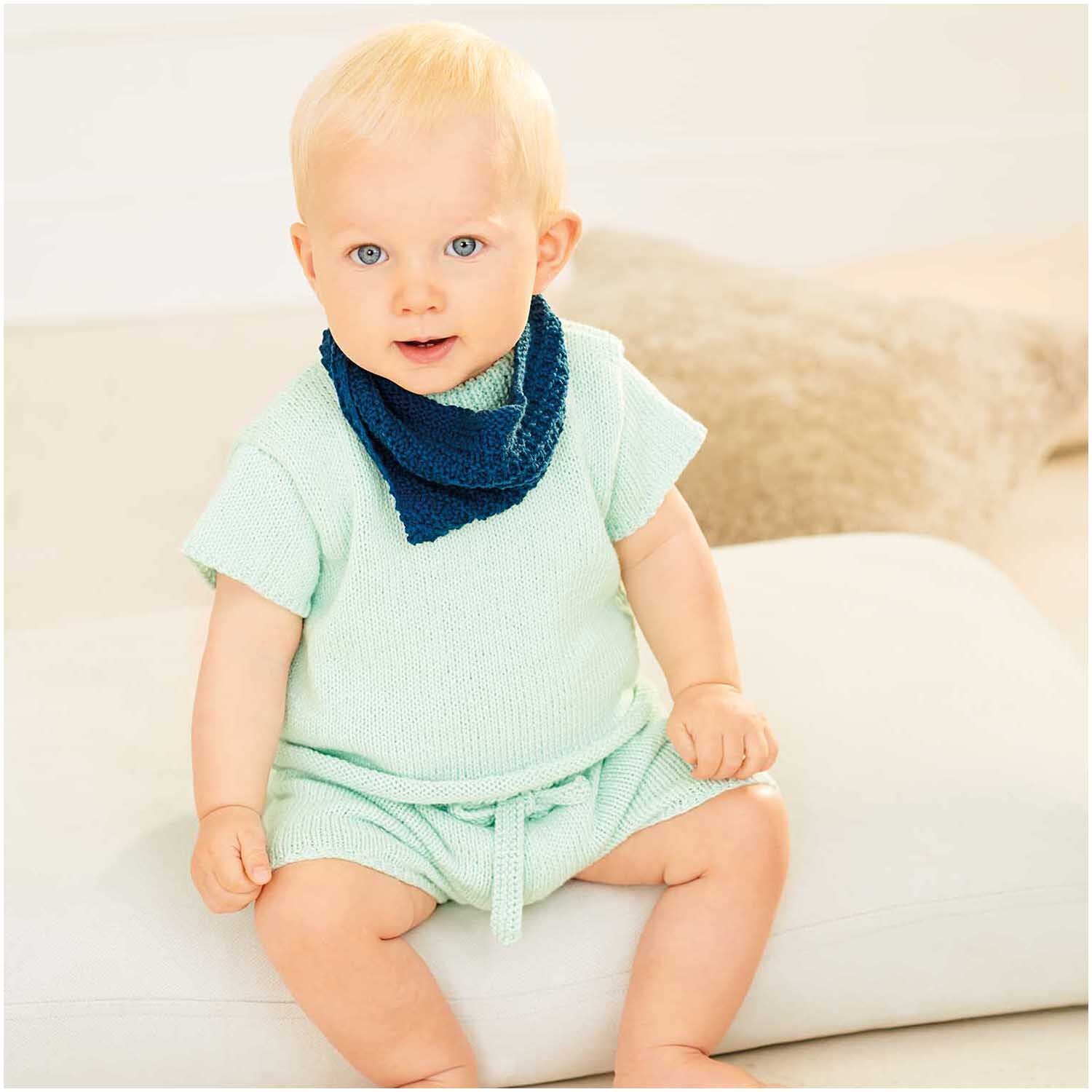 Baby Organic Cotton: Ein Baby trägt ein mintgrünes Outfit mit marineblauem Halstuch, sitzt auf einem weißen Kissen.