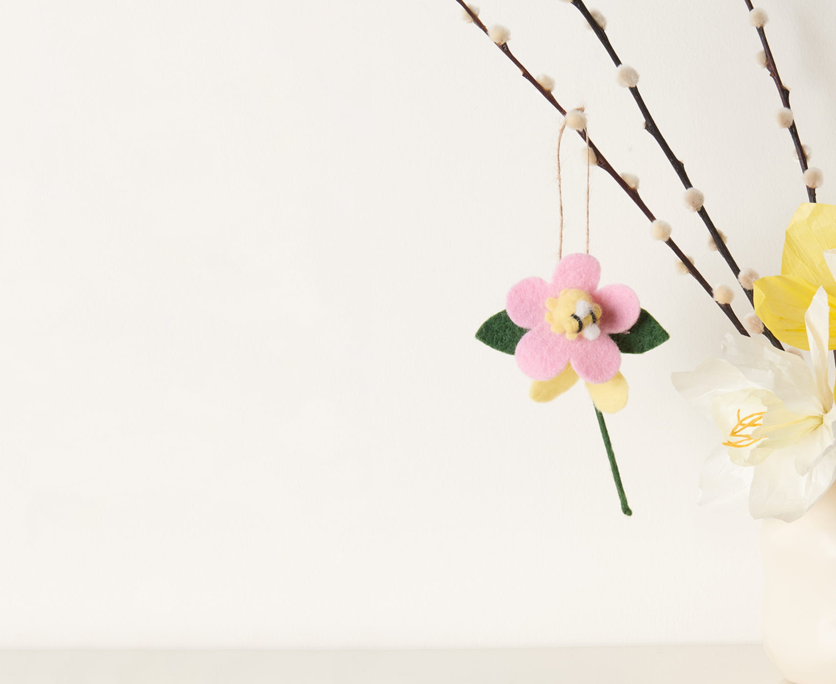 Eine Filz-Blume mit Biene hängt dekorativ an Zweigen.