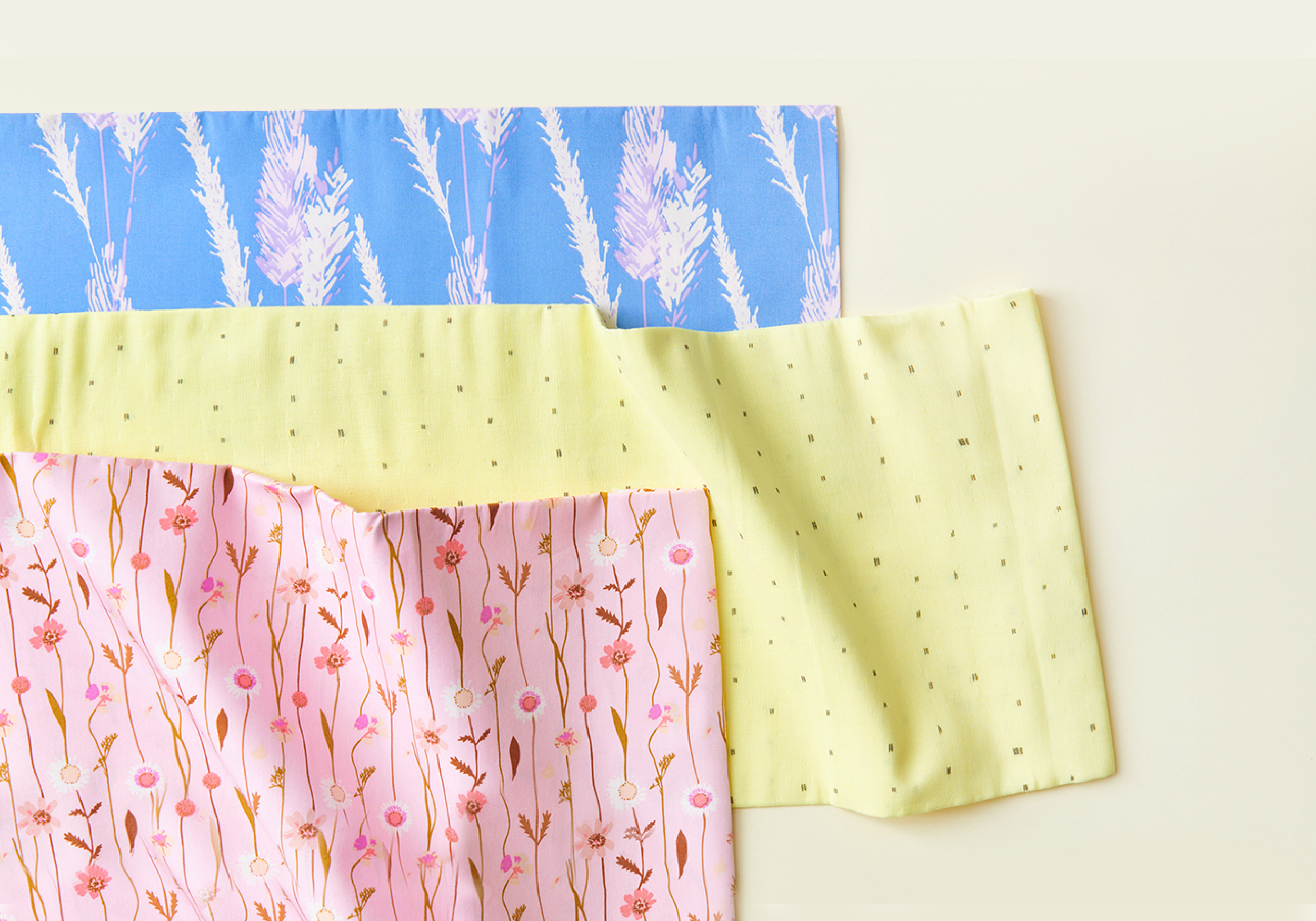 Stoffbahnen in blau, gelb und rosa mit floralem Print liegen auf gelbem Hintergrund