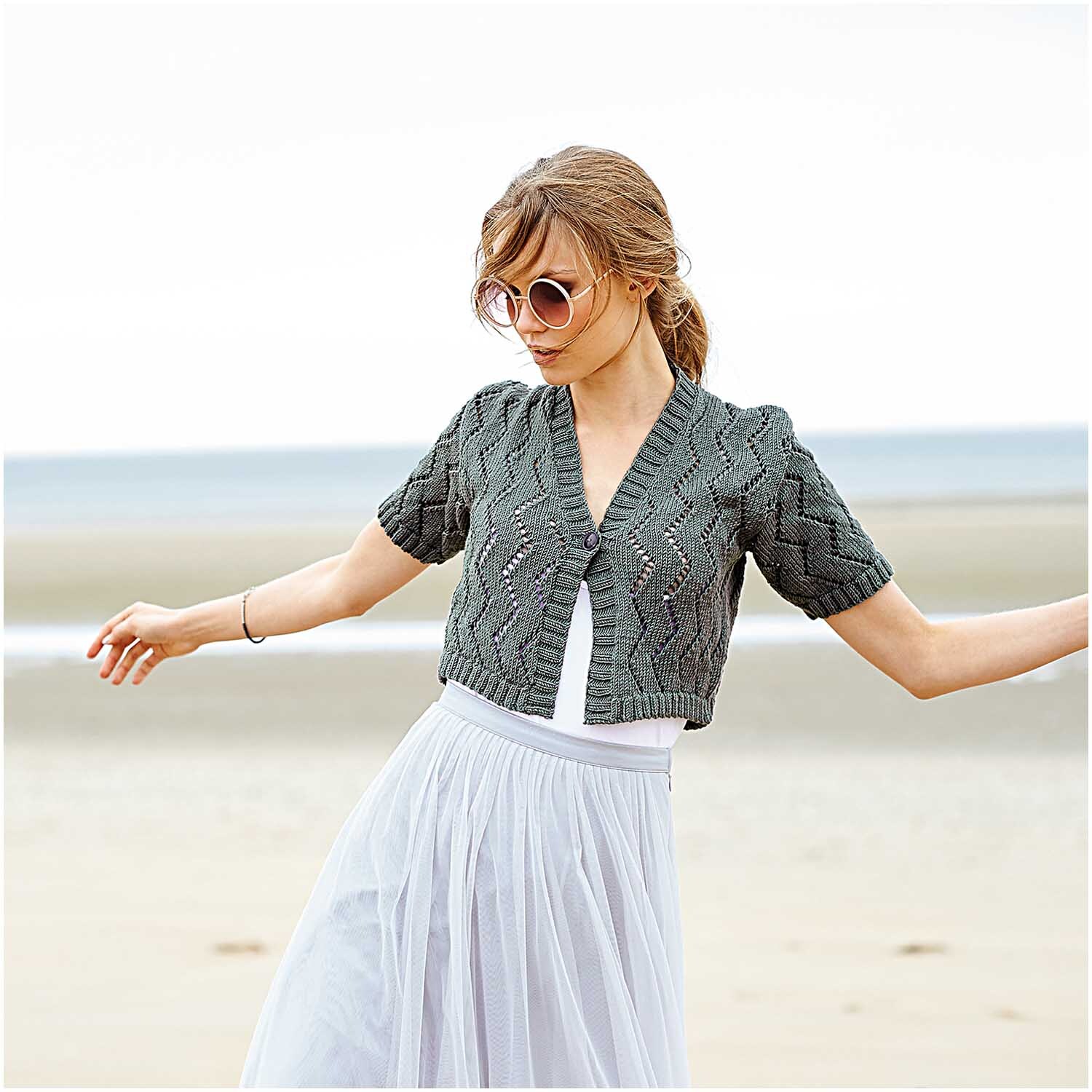 Creative Silky Touch dk: Frau am Strand in gestrickter olivgrauer Jacke von Rico Design, luftig und stilvoll.