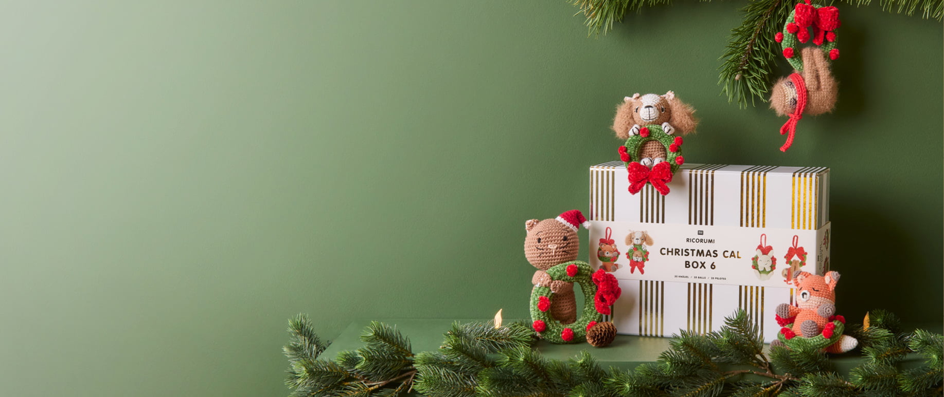 Ricorumi Xmas CAL Box 5 steht vor dunkelgrünen Wänden und ist umgeben von Häkelfiguren.