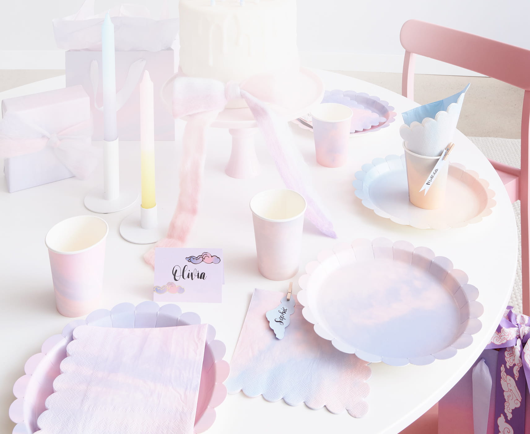 Ein Tisch ist in Pastelltönen mit Pappteller, -becher, Servietten und Dekoration gedeckt.