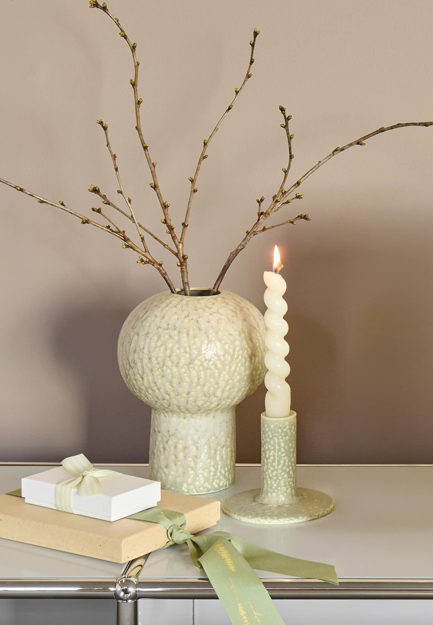 Eine Vase und ein Kerzenständer stehen dekorativ auf einem weißen Regal vor einer beigen Wand. 