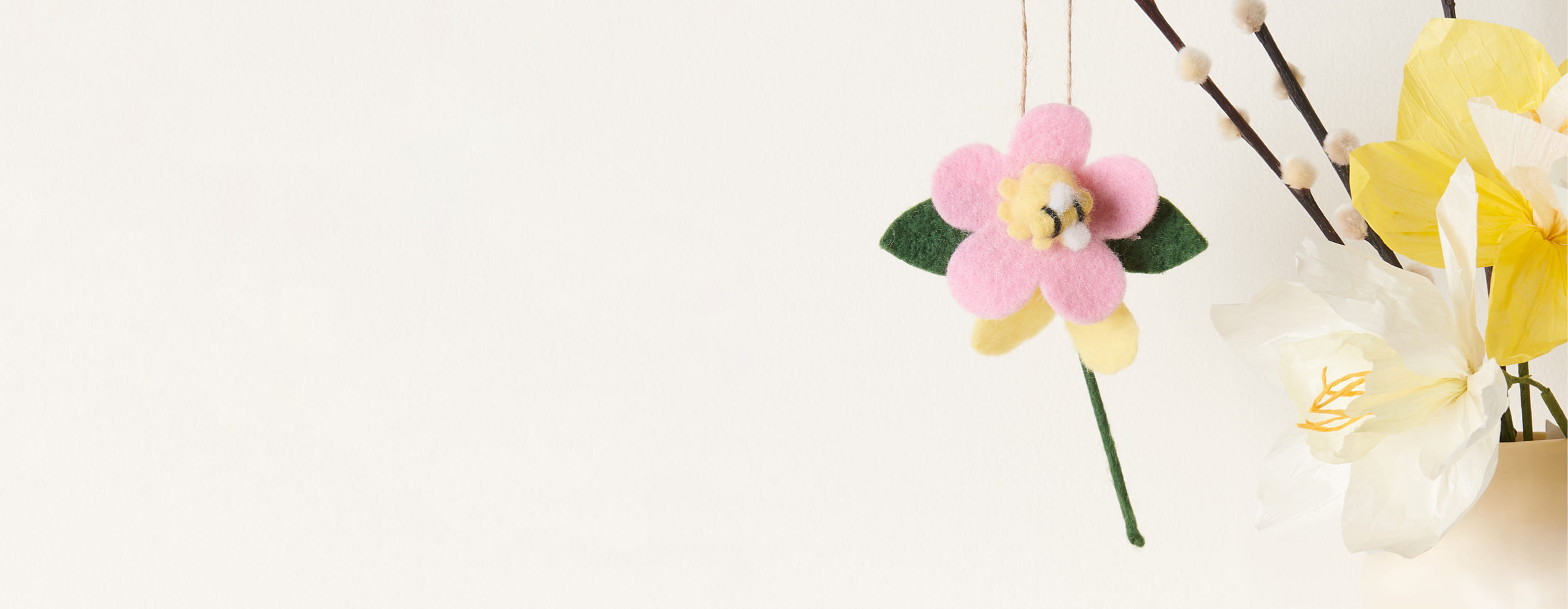 Eine Filz-Blume mit Biene hängt dekorativ an Zweigen.