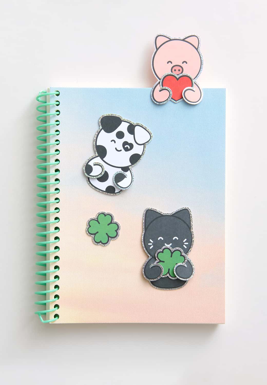 Clip-Ons in Form von Dalmatiner, Katze und Schwein schmücken ein Notizheft. 