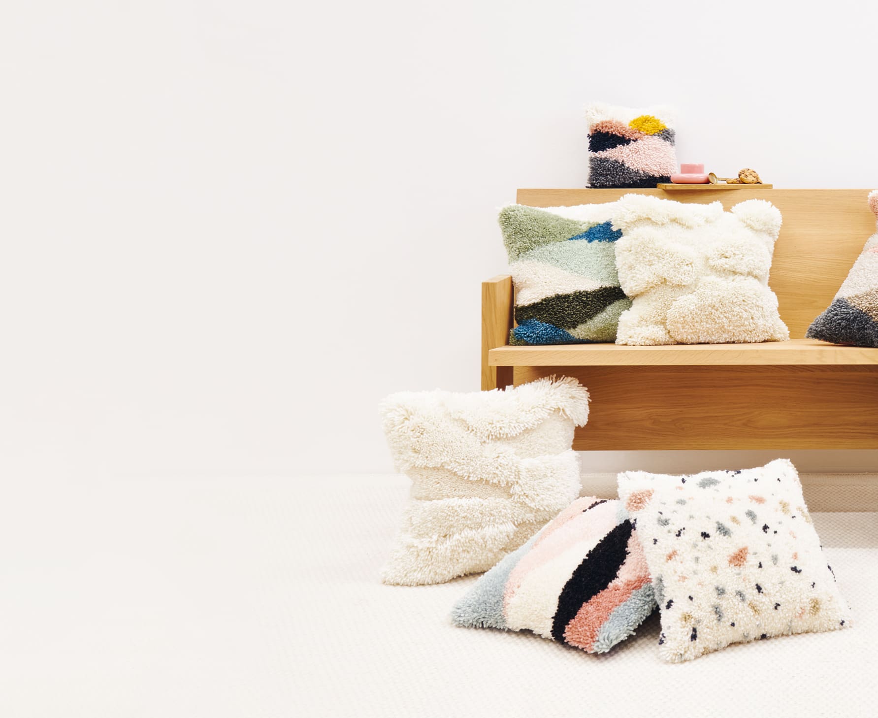 Geknüpfte Kissen mit abstrakten Designs liegen verteilt vor und auf einer Sitzbank. 