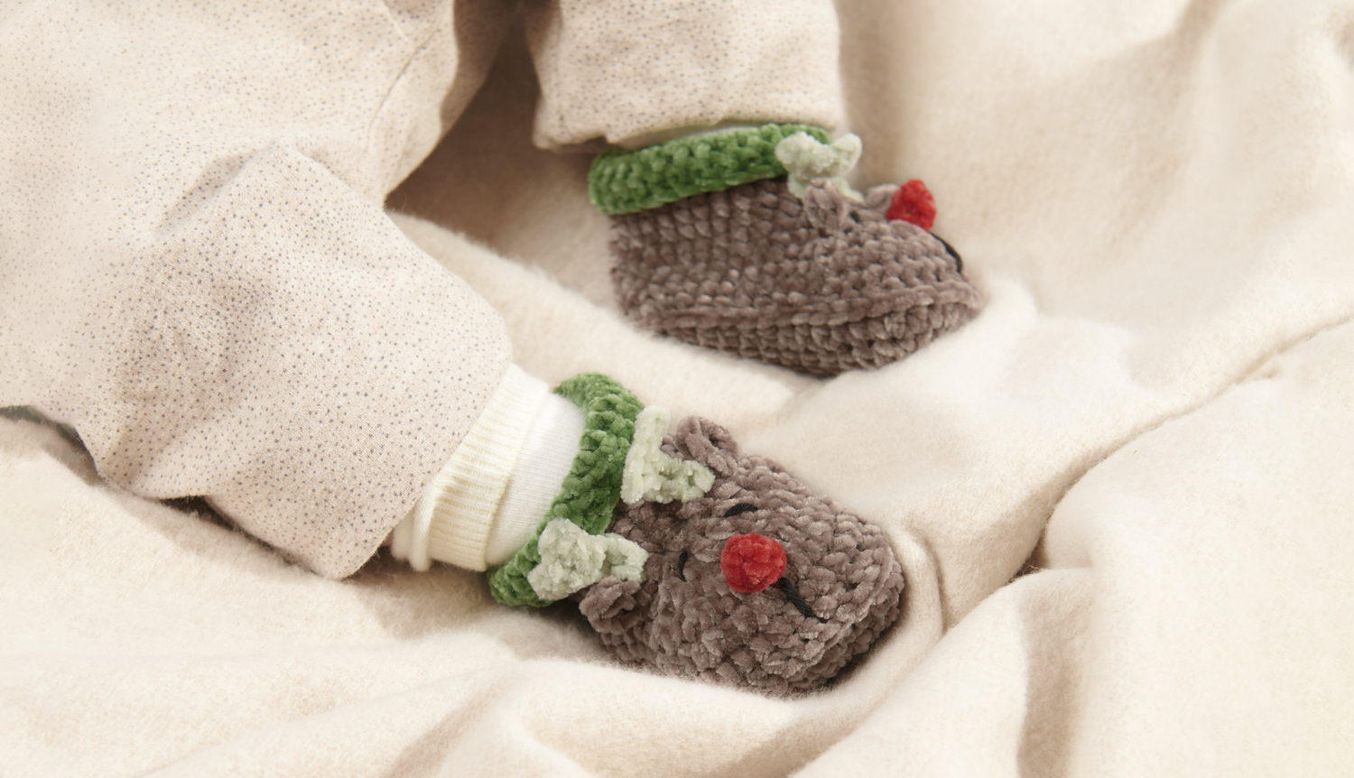 Häkelanleitung Baby Booties Rentier Häkelanleitung Baby Booties Rentier: Niedliche braune Babyschuhe mit Rentiermotiv und grünen Details auf beigem Stoff.
