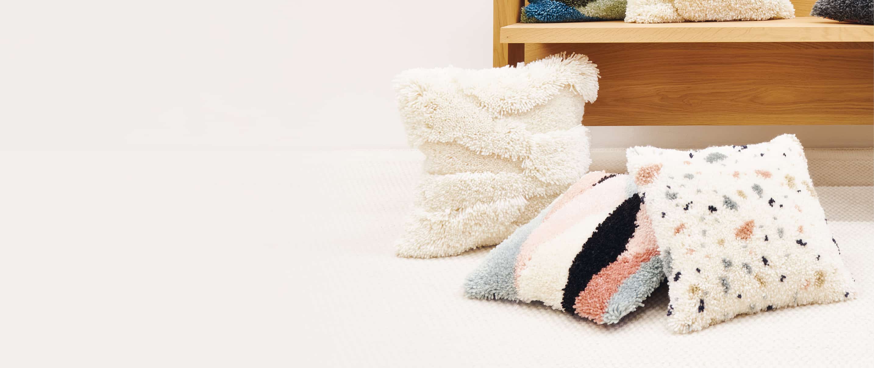 Geknüpfte Kissen mit abstrakten Designs liegen verteilt auf einem hellen Teppich.