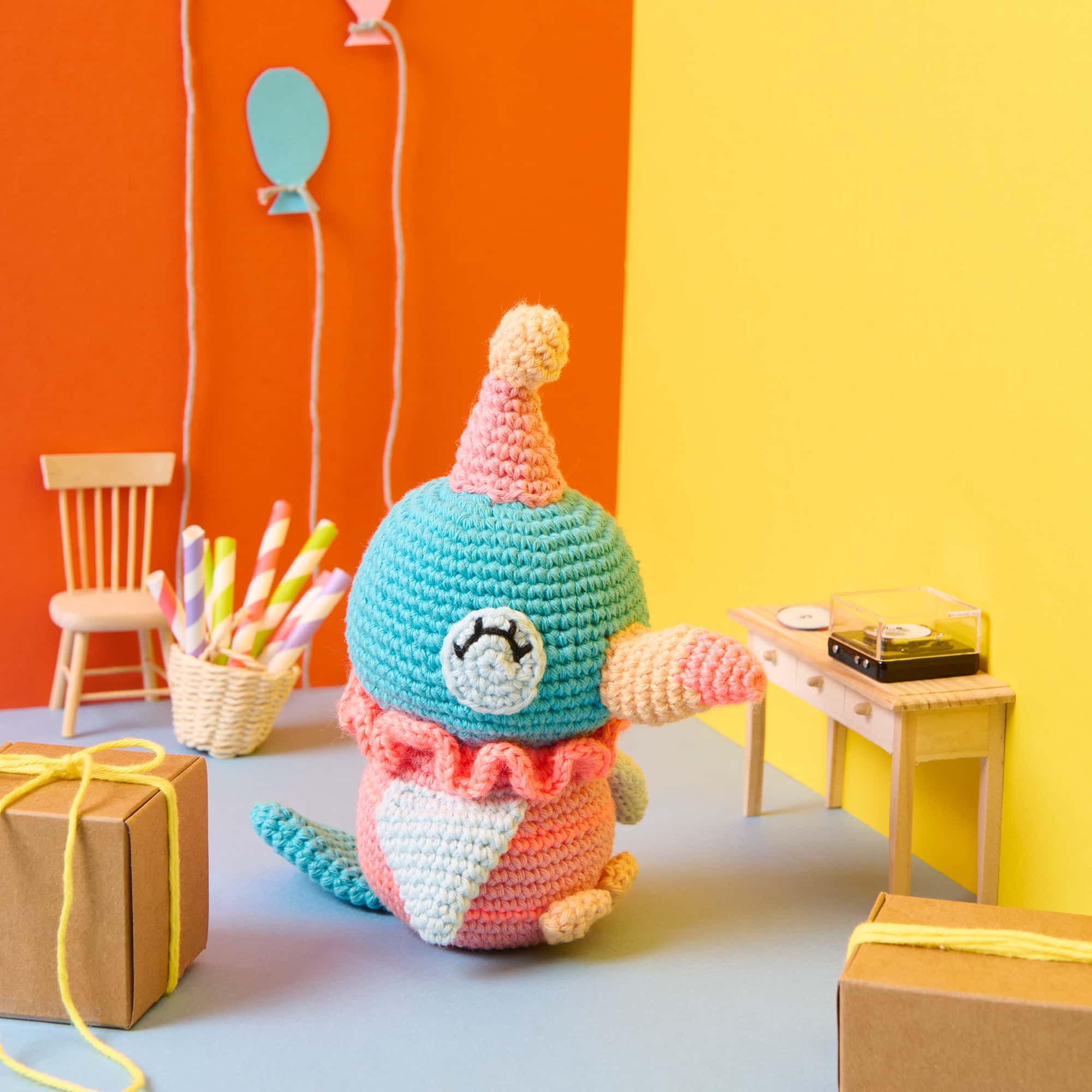 Ein gehäkelter Toucan mit Partyhut sitzt in einer bunt dekorierten Szene mit Partydekoration.