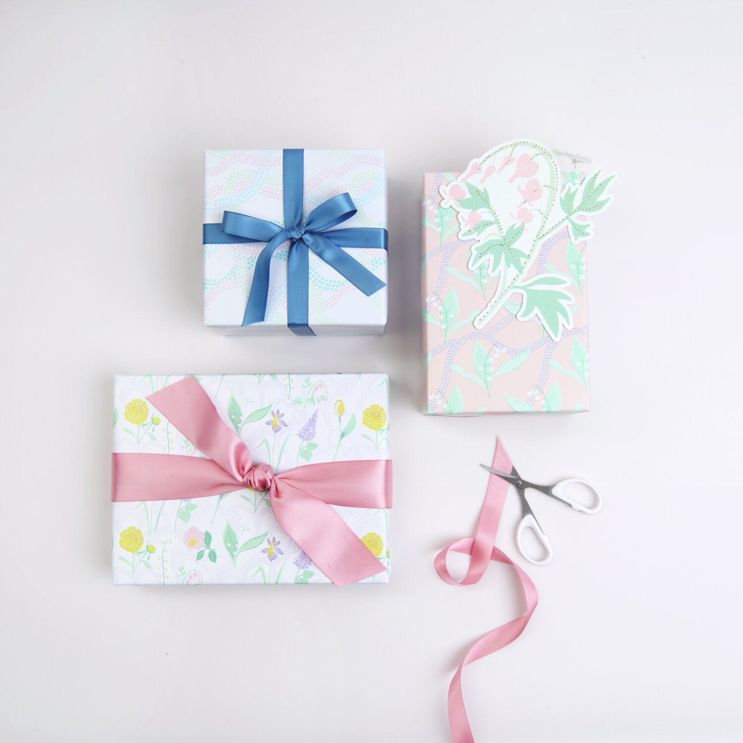 Paper Poetry Geschenkpapier Mix Blumenwiesen, dekoriert mit rosa und blauen Schleifen, auf weißem Hintergrund.