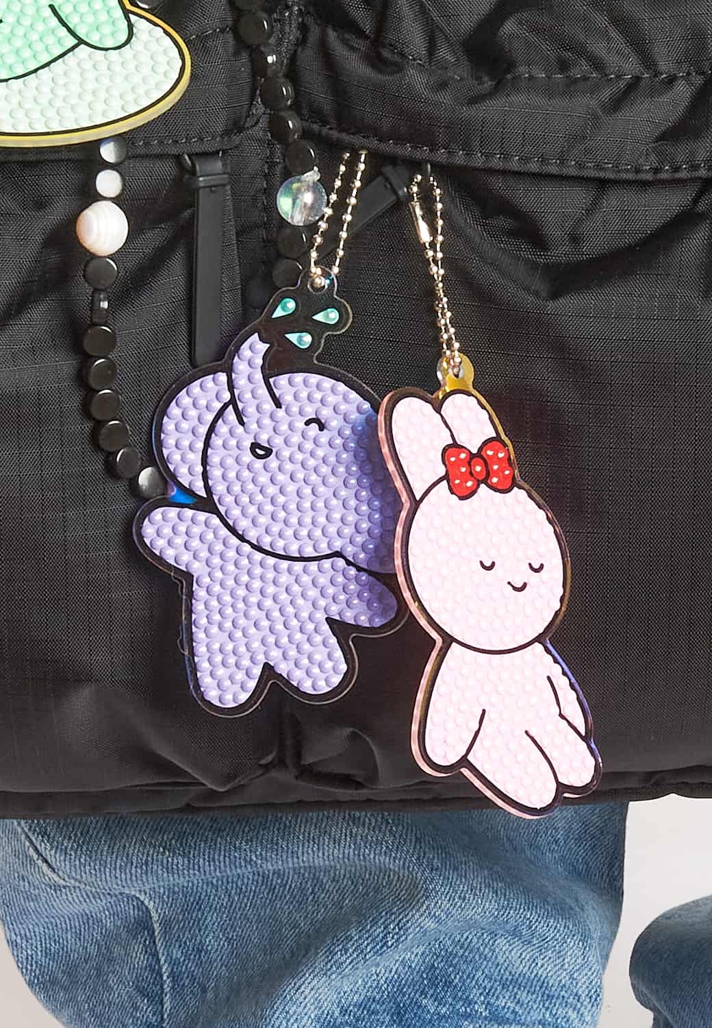 Diamond Painting Anhänger in Form eines Elefanten und eines Hasen hängen dekorativ an einer Tasche.