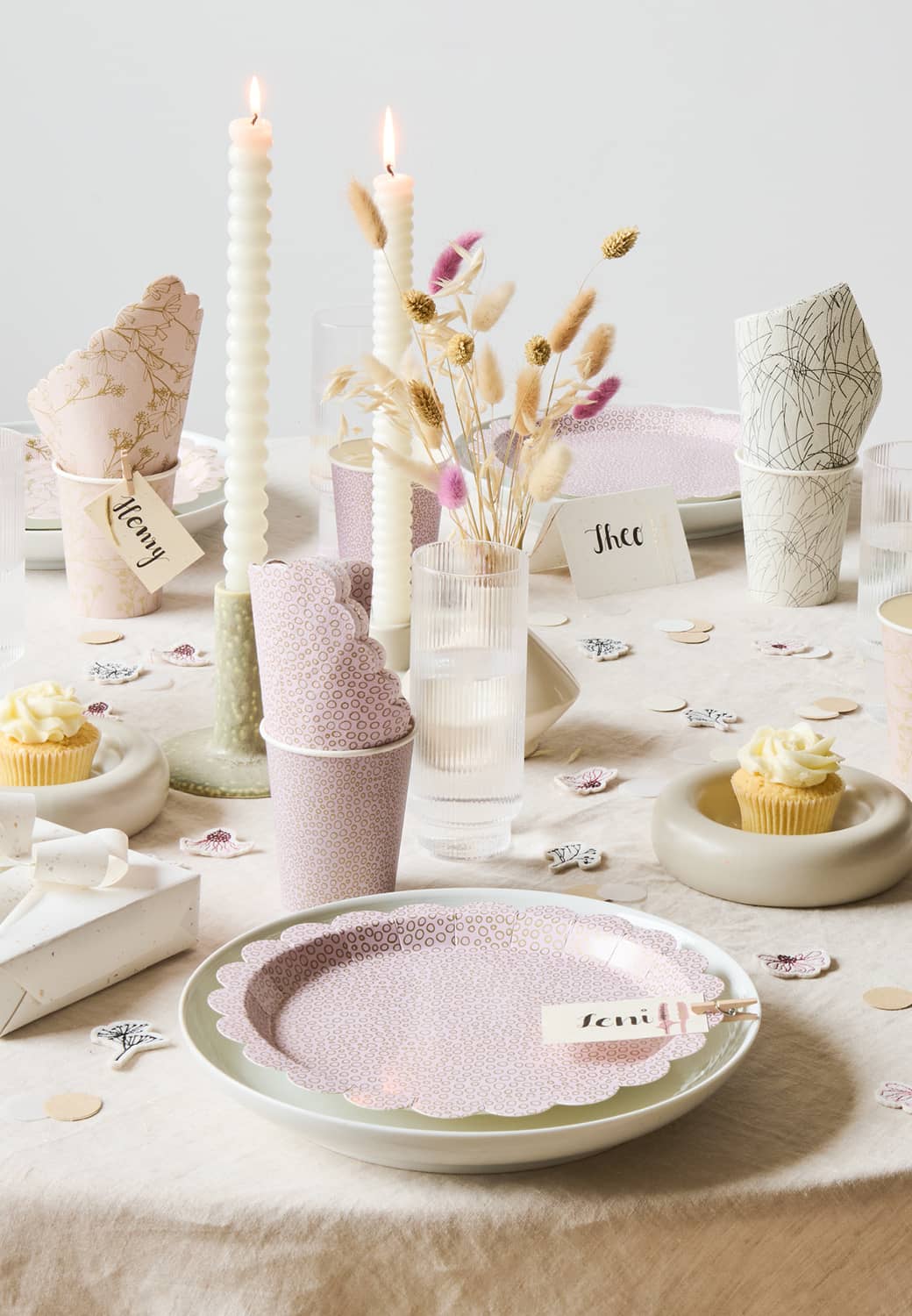Ein Tisch ist mit Pappgeschirr, Filzstreu, Kerzen und Trockenblumen in Natur- und Pastelltönen geschmückt. 