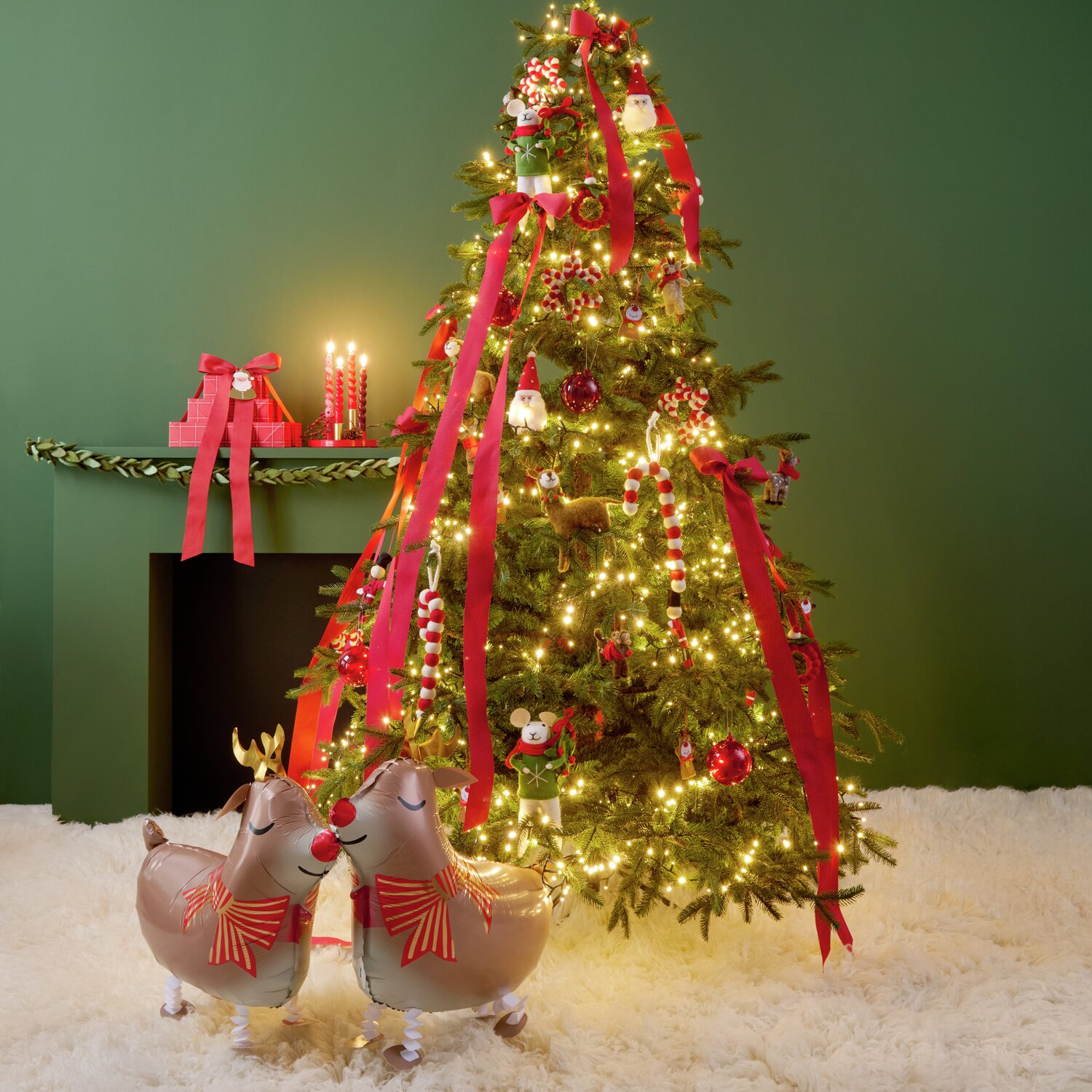 Filz-Hirsch mit Ilexkranz in Braun von Rico Design vor einem festlich geschmückten Weihnachtsbaum. Der Baum ist mit roten Bändern und Lichtern dekoriert. Perfekt für weihnachtliche Dekorationen.