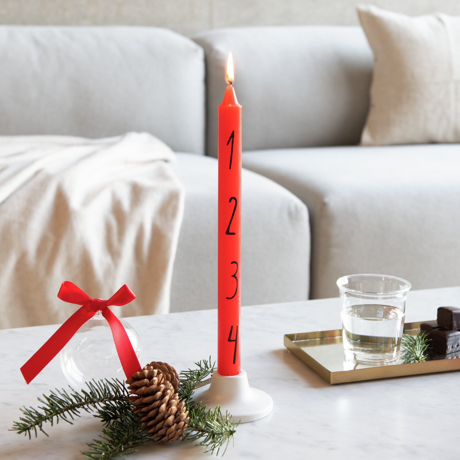 Adventskerze Zahlen 1-4, rot, Ø2,2x28cm, brennend auf Tisch mit Tannenzweig und Schleife.