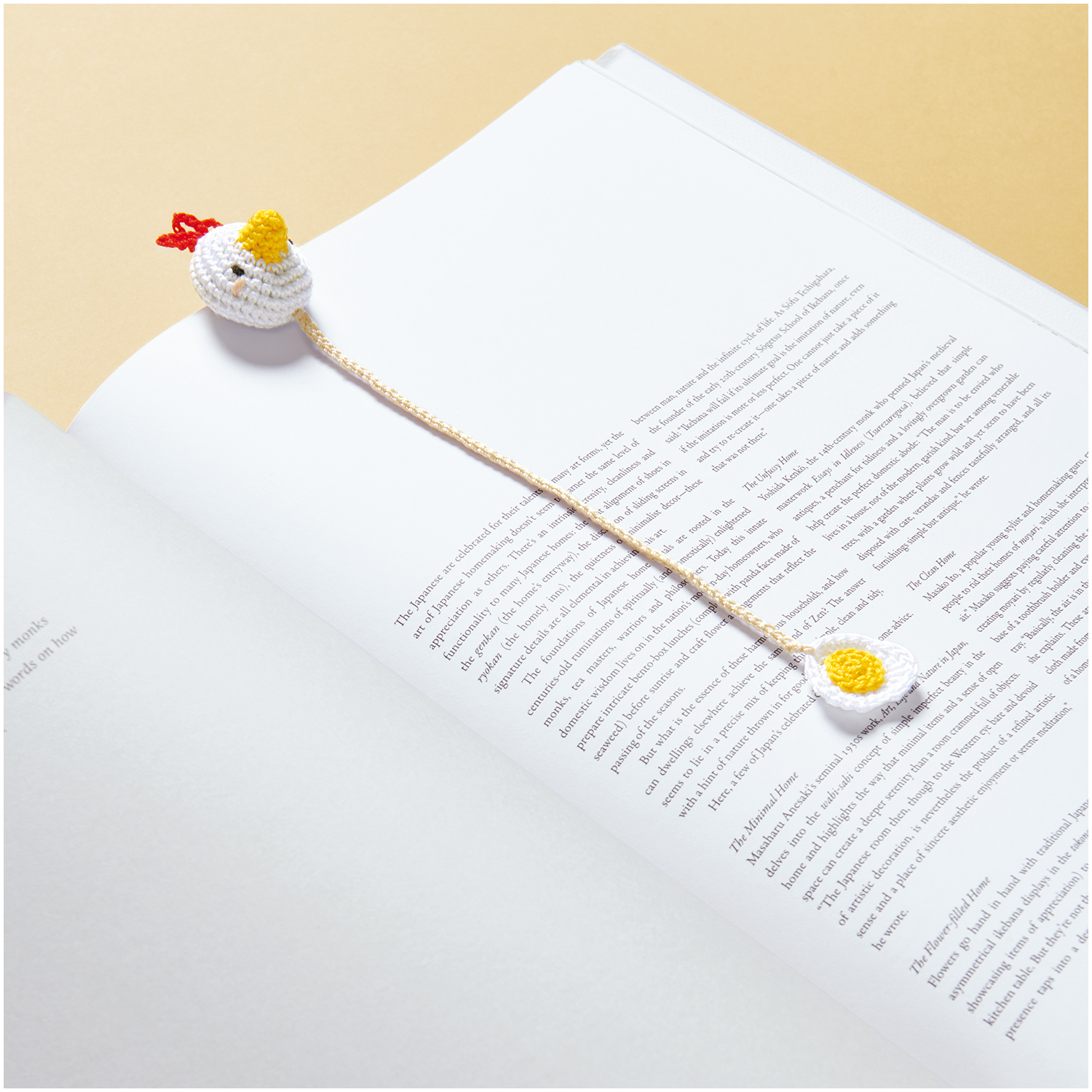 Essentials Crochet: Ein gehäkeltes Lesezeichen in Form eines Huhns liegt auf einem offenen Buch.
