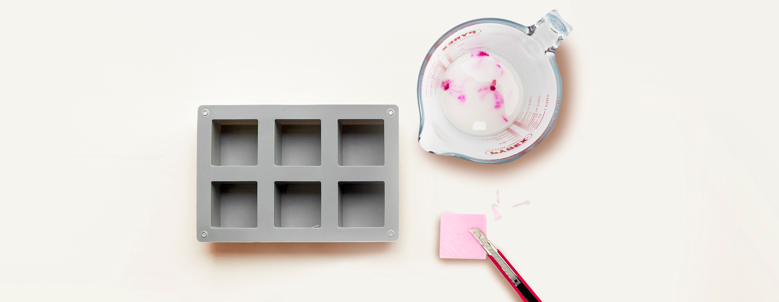 Seifengießform, ein rosa Seifenstück und ein Messbecher mit geschmolzener Seife