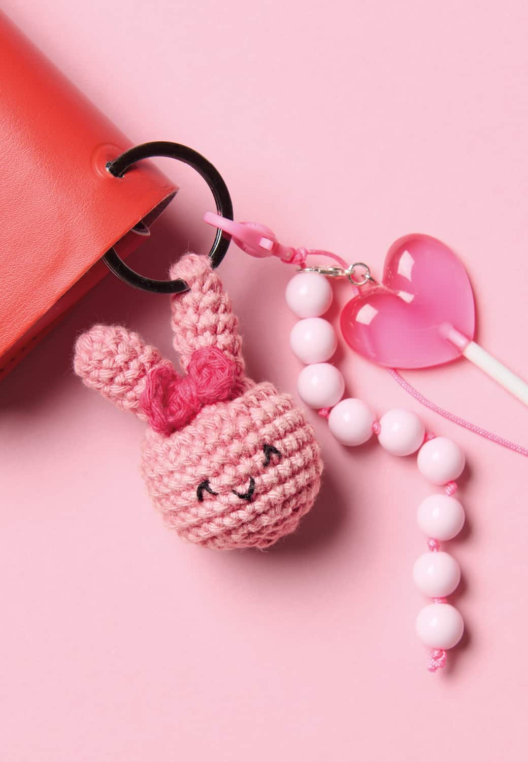 Ein gehäkelter Hasenkopf an einem Schlüsselring liegt auf rosa Hintergrund. 