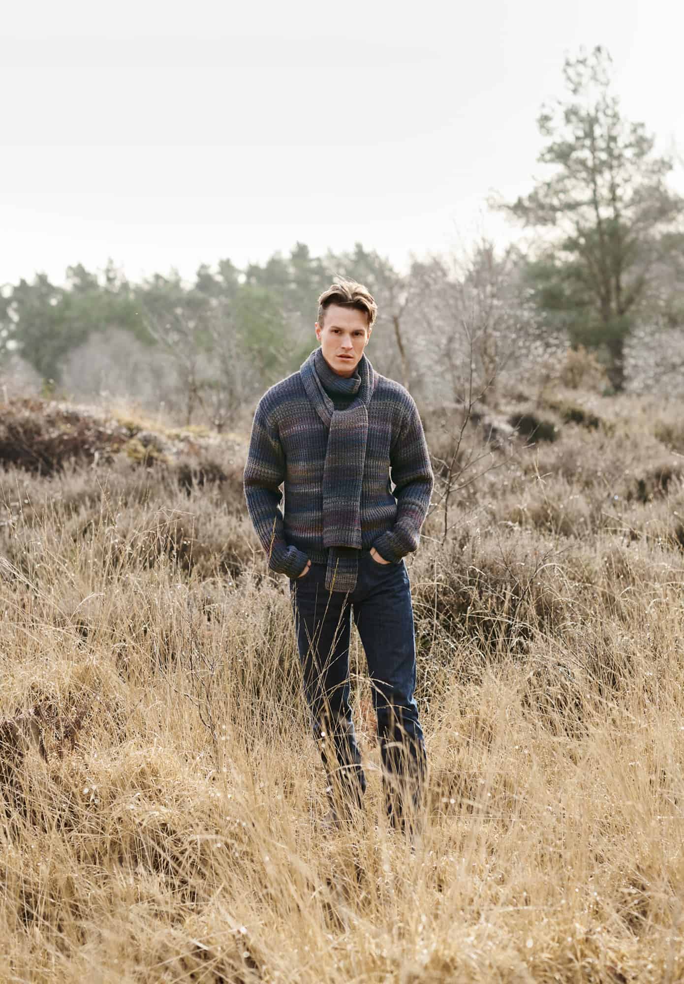 Mann trägt gestrickten Pullover mit Farbverlauf in dunklen Braun, Lila und Blautönen: Modell 24 aus Lovewool No. 21