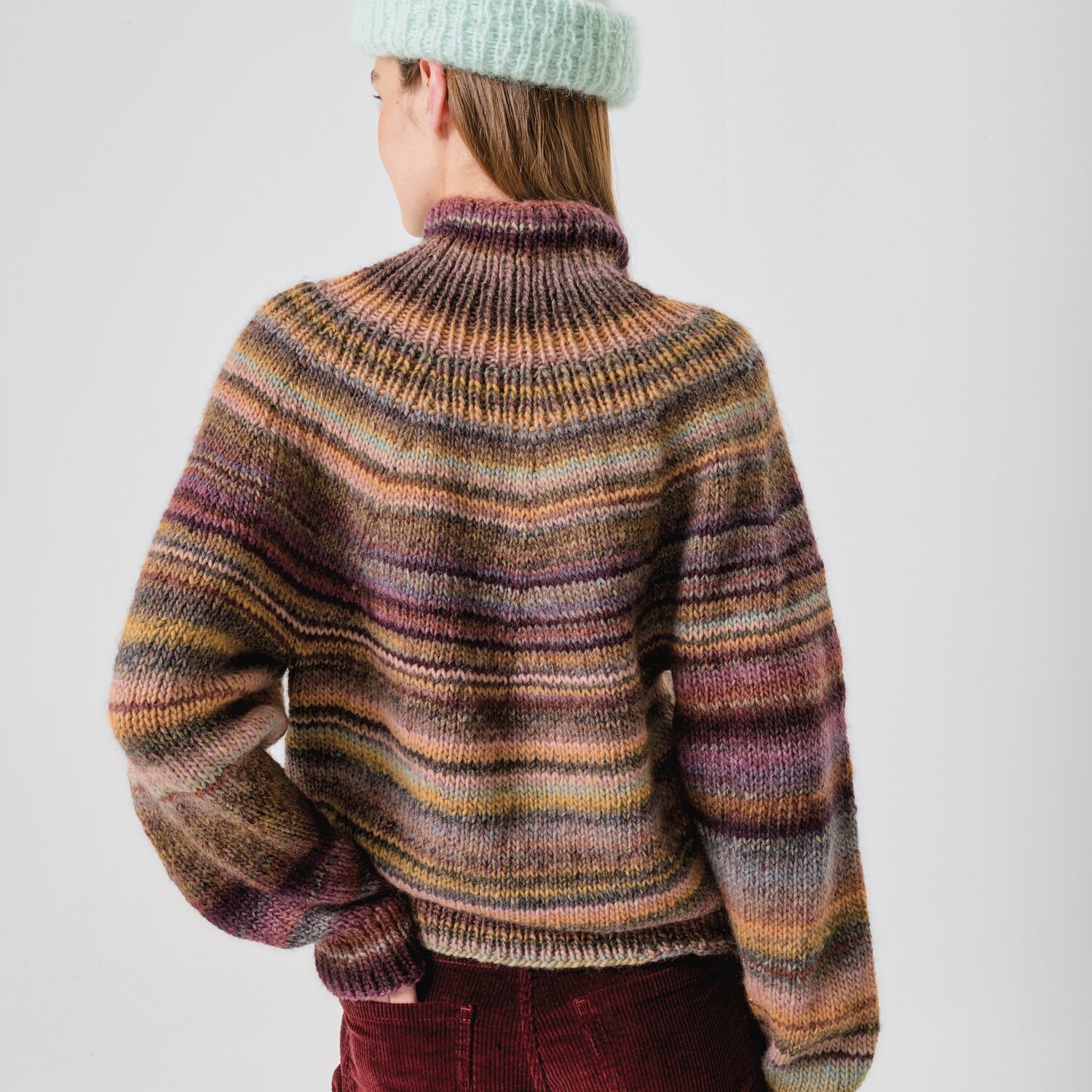 Strickset Pullover Modell 26 aus Made by Me No. 21 von Rico Design Strickset Pullover Modell 26 aus Made by Me No. 21, gestreift in Erdtönen, getragen von Person mit mintgrüner Mütze.
