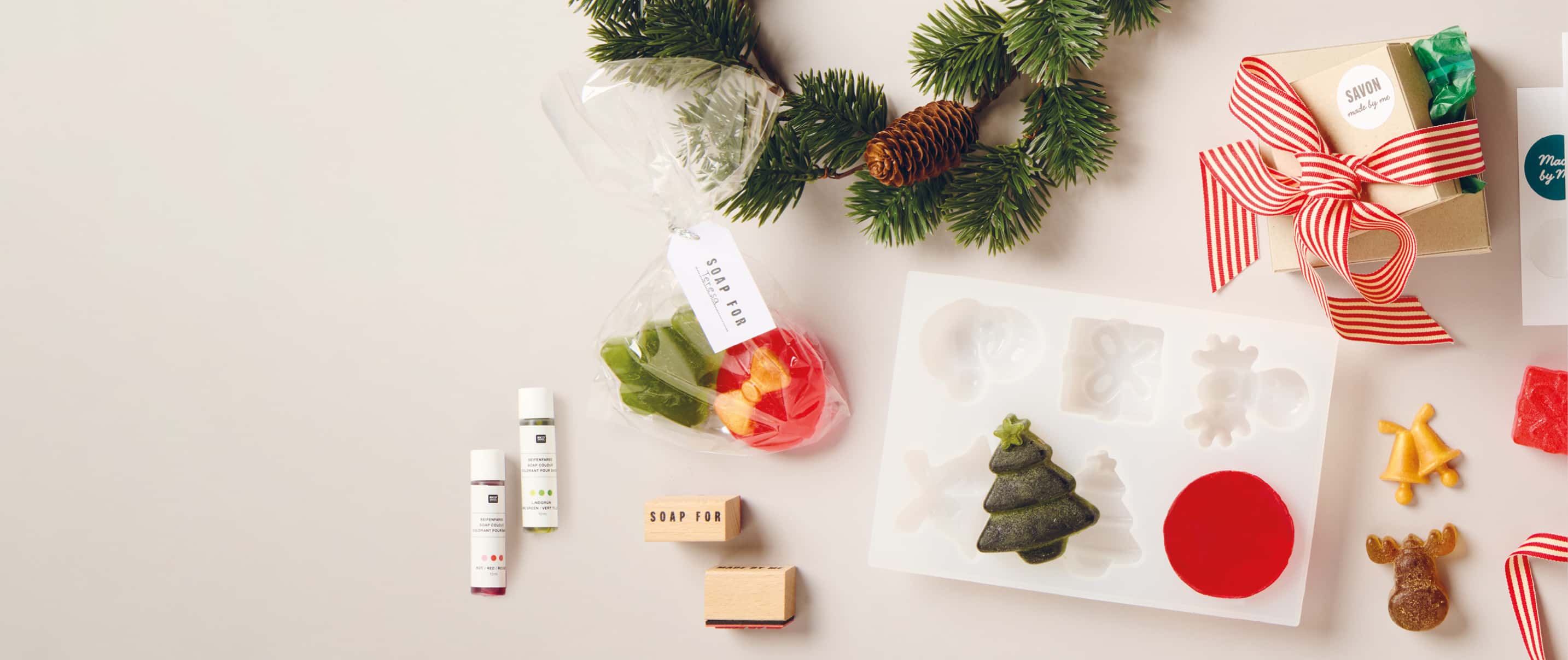 Selbstgemachte Seifen in Weihnachtsformen liegen mit Silikonform, Seifenzubehör und Geschenkverpackungen auf hellem Untergrund.