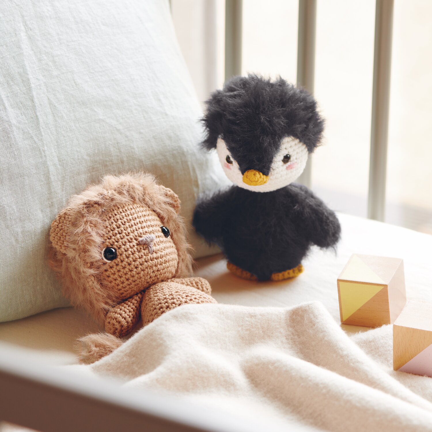 Ricorumi Furry Animals: Kuscheltier-Löwe in Karamell und Pinguin in Schwarz auf Bett mit Holzklötzen.