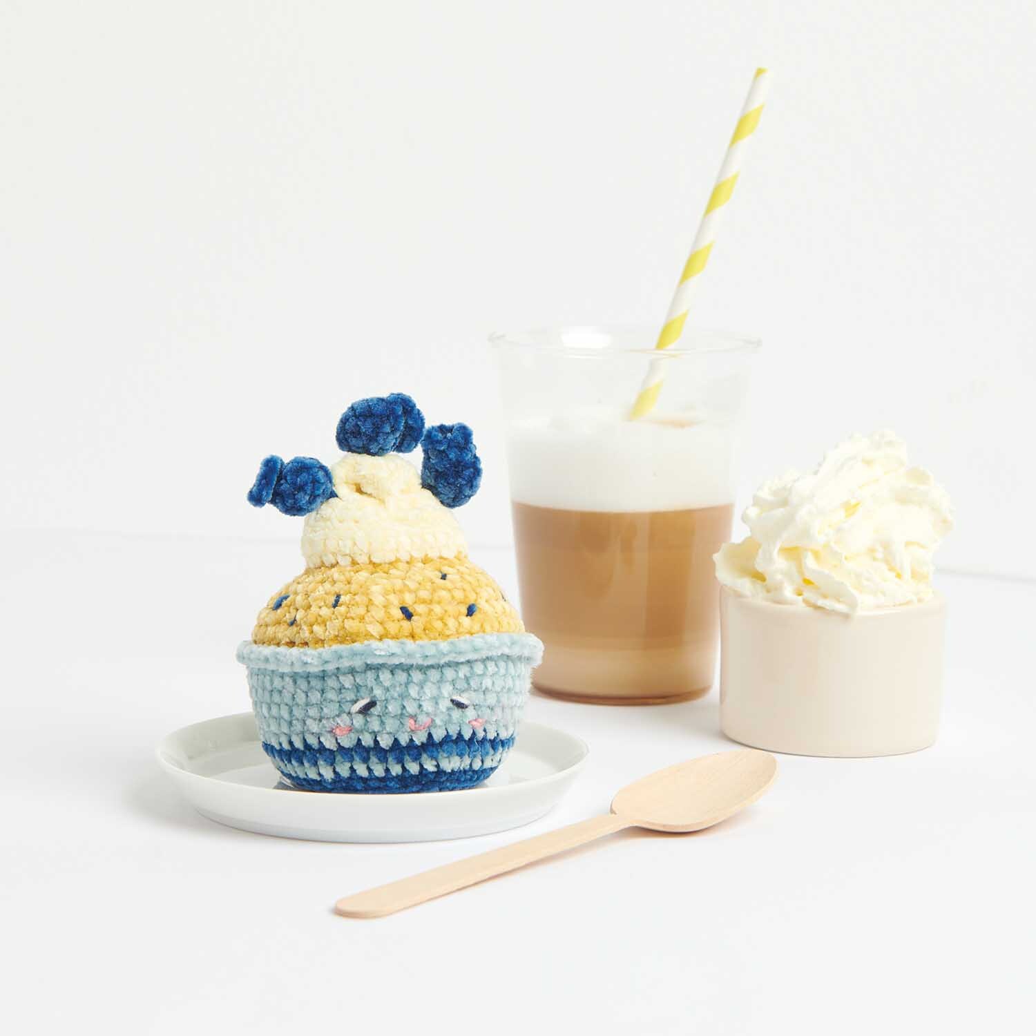 Häkelanleitung Blueberry Cupcake: Ein gehäkelter Cupcake mit blauen Beeren, neben einem Latte und Sahne.