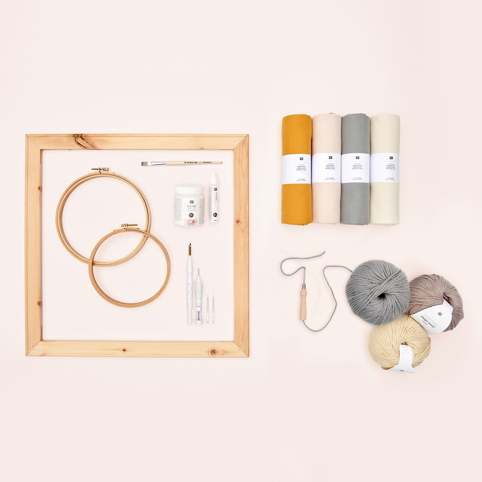 Punch Needle, Stickrahmen, Stoffrollen und Garn liegen auf rosa Untergrund.