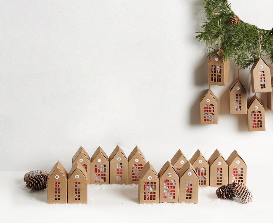 Adventskalender in Form von Papphäusern sind weihnachtlich aufgestellt und an einem Kranz dekoriert