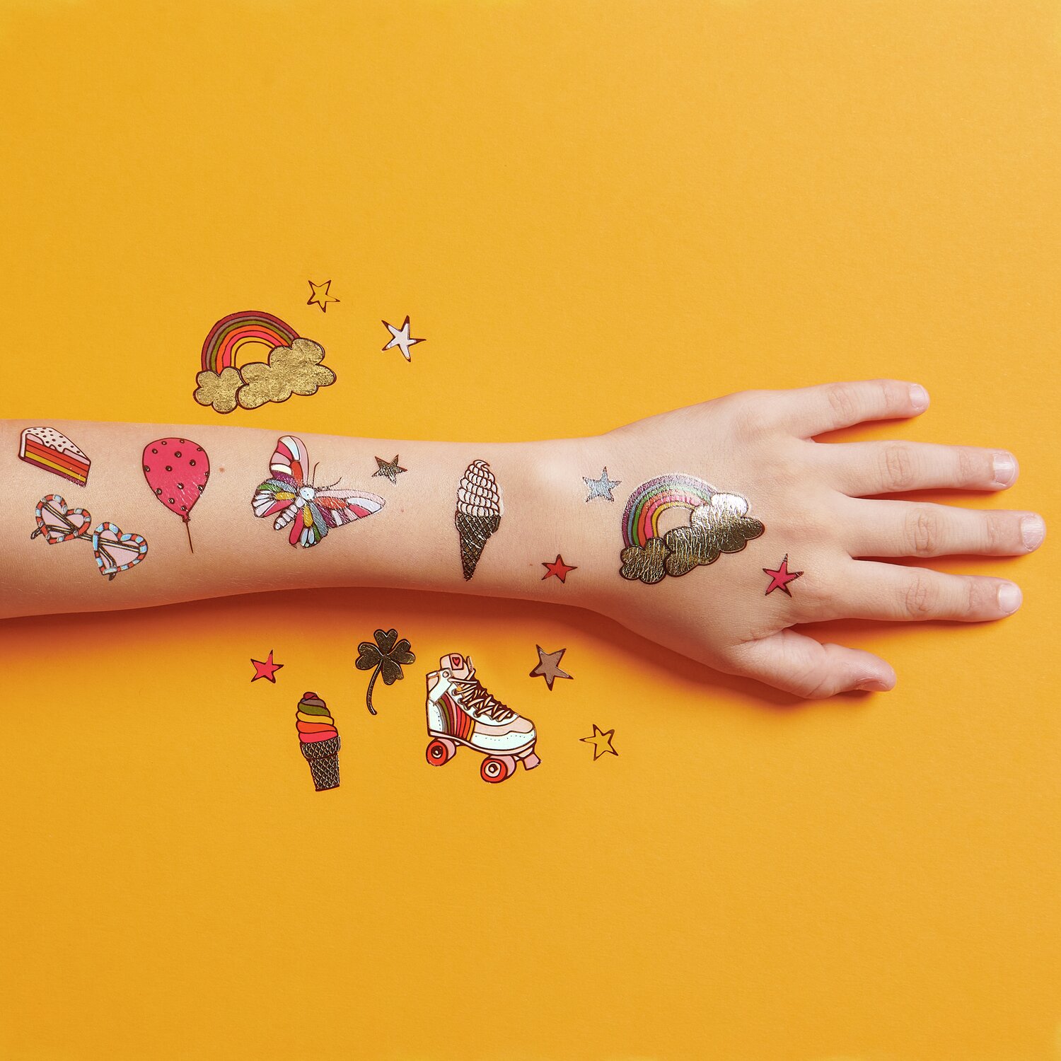 Tattoos Rainbow Fun: Bunte, temporäre Tattoos auf einem Arm, 19-teilig, auf orangefarbenem Hintergrund.