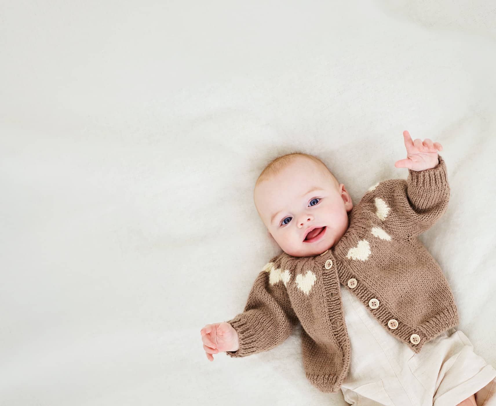 Ein Baby liegt mit einer Strickjacke gekleidet auf einer Decke.