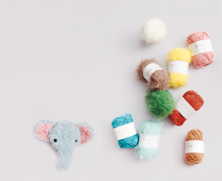Bunte Knäuel von Ricorumi dk und Ricorumi Furry Furry und ein gehäkelter Elefant liegen verteilt auf grauem Hintergrund.