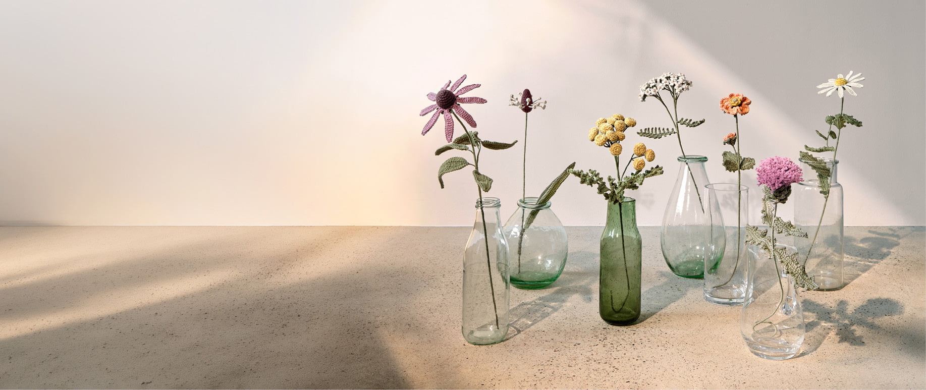 Gehäkelte Wiesenblumen stehen dekorativ in Glasvasen. 