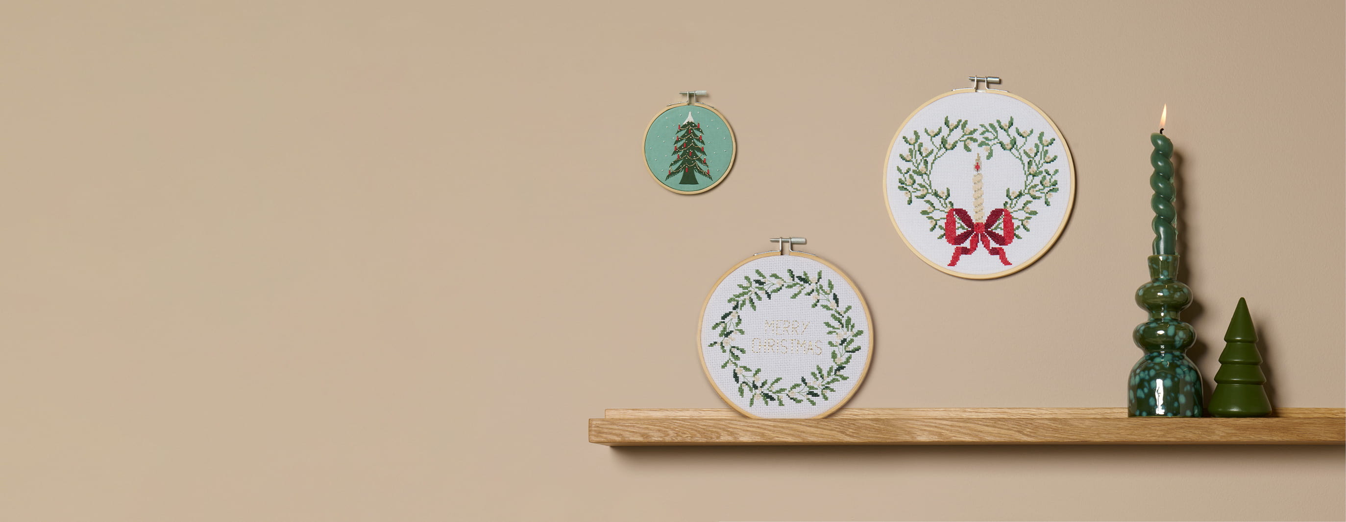 Weihnachtliche Kreuzstichmotive in Stickrahmen mit Tannenbaum, Kerzenkranz und Schriftzug „Merry Christmas“ als Wanddekoration.