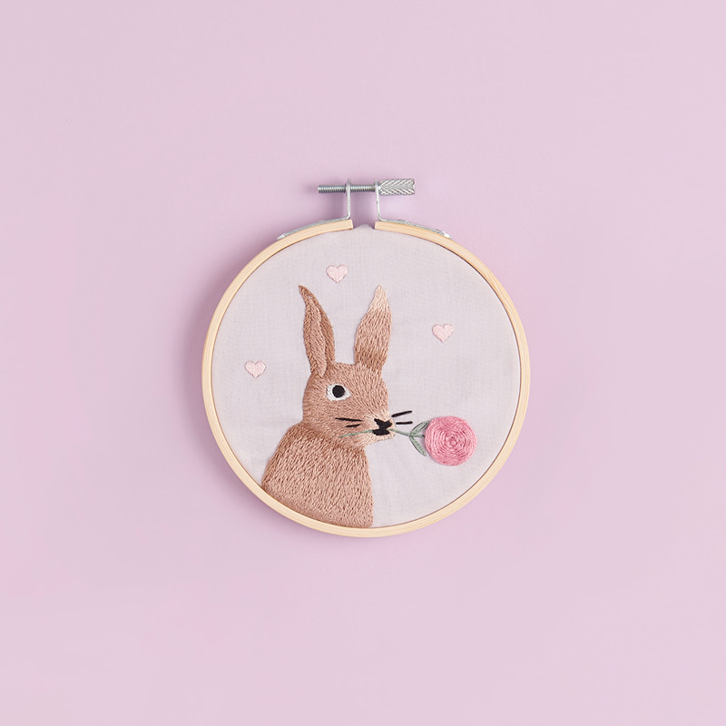 Gesticktes Bild mit Hase liegt auf rosa Hintergrund.