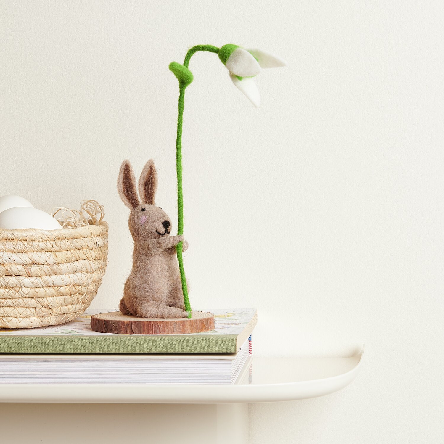 Filz-Hase mit Schneeglöckchen: Niedliche Dekofigur aus Filz, hält ein Schneeglöckchen, auf einem Tisch platziert. Ideal für Frühlingsdekoration.