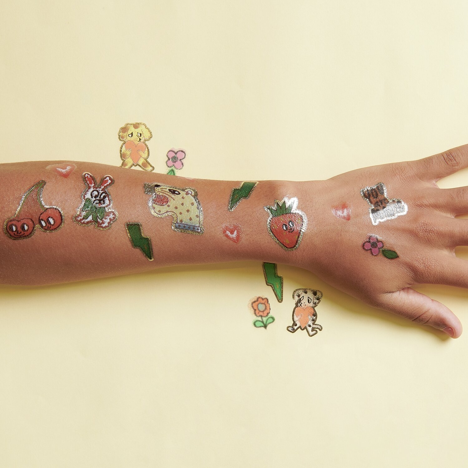 Tattoos Früchte und Tiere: Temporäre Tattoos auf einem Arm mit bunten Motiven wie Kirschen, Erdbeeren und Tieren. 16-teiliges Set.