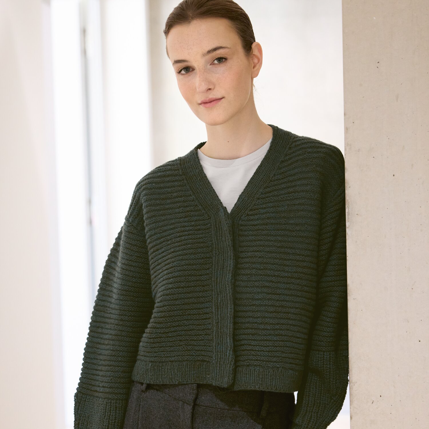 Strickset Jacke Modell 16 aus Luxury Knits: Dunkelgrüne Strickjacke aus Premium Natural Fibres, getragen von einer Frau vor hellem Hintergrund.