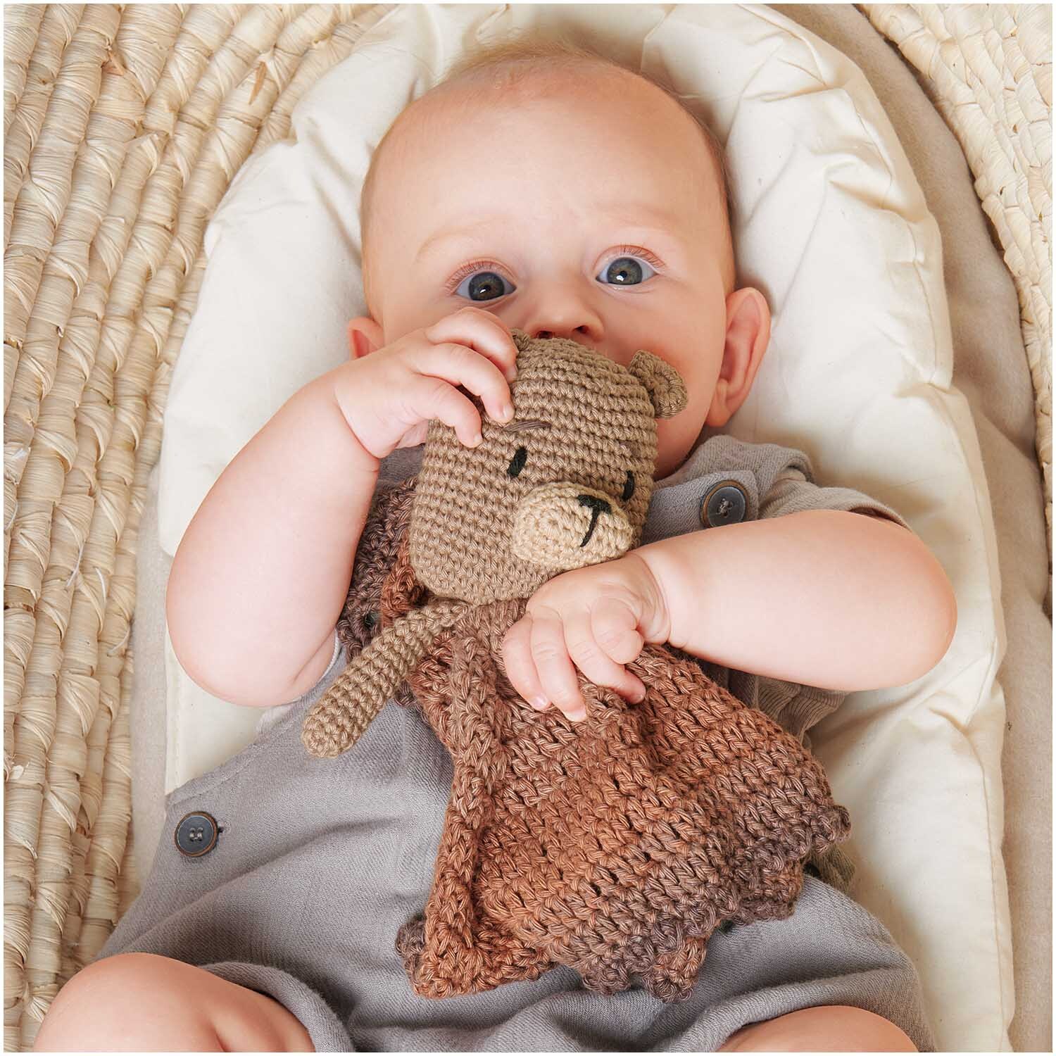 Ricorumi Spin Spin dk: Ein Baby hält ein braunes, gehäkeltes Kuscheltier von Rico Design in den Händen.