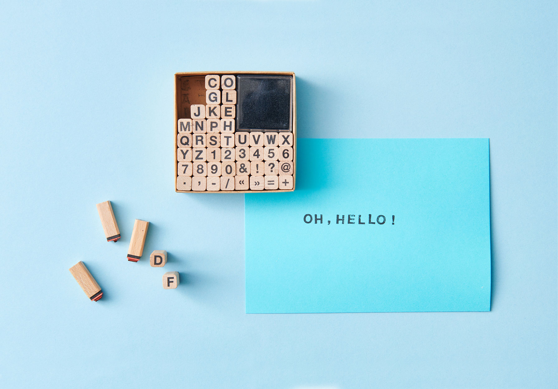 Blaue Karte mit gestempeltem Text "Oh, hello!", daneben ein Stempelset mit Buchstaben und Zahlen auf blauem Hintergrund