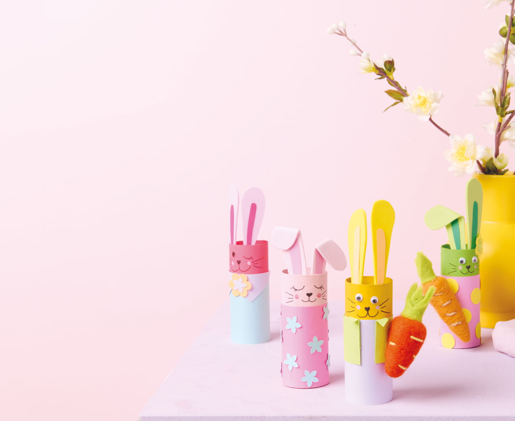 Bunte Hasenfiguren aus Papierrollen stehen vor einem rosa Hintergrund.