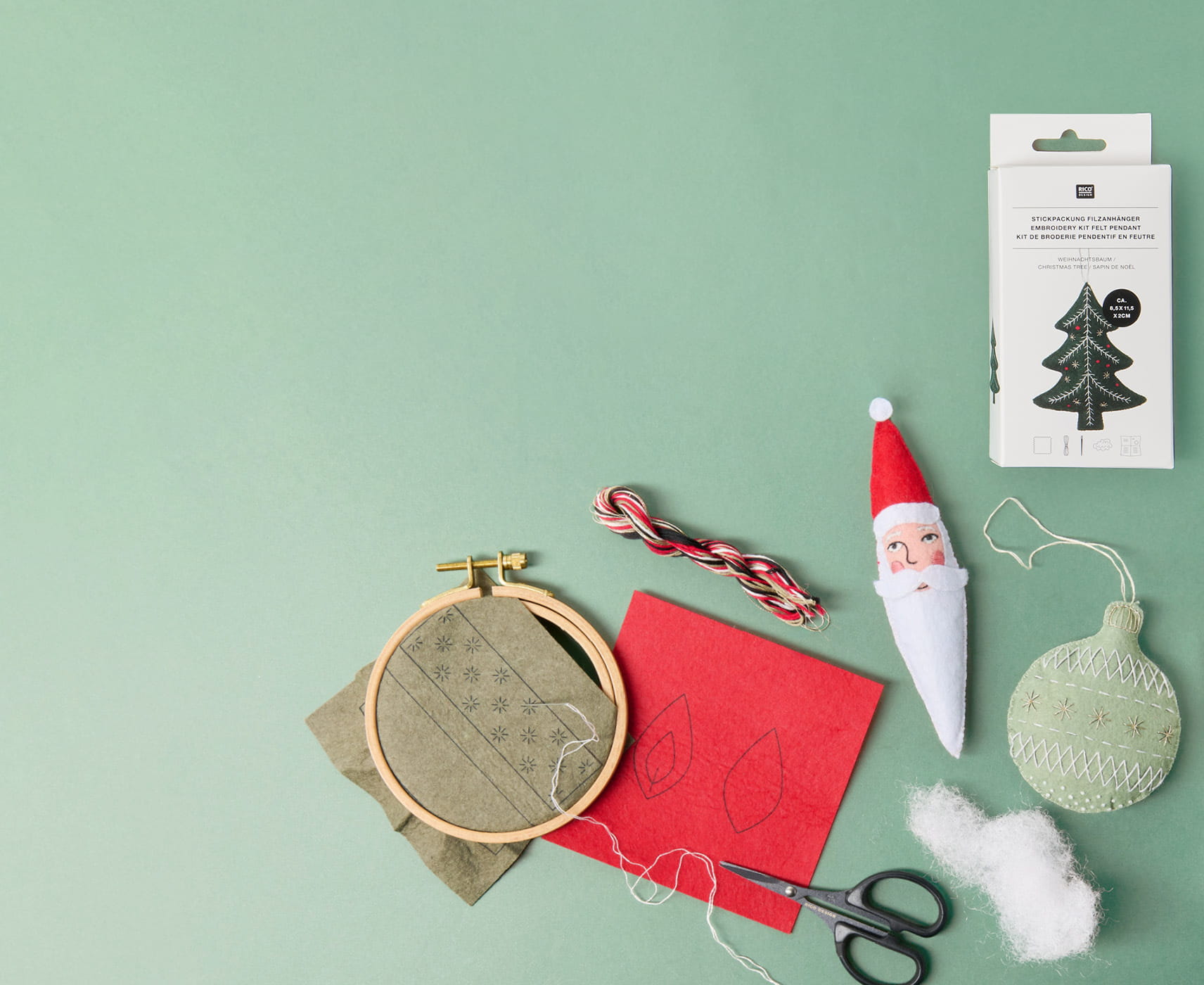 Materialien für gestickte Filzanhänger mit Weihnachtsmotiven, darunter Stickrahmen, Garn, Schere und fertige Anhänger.