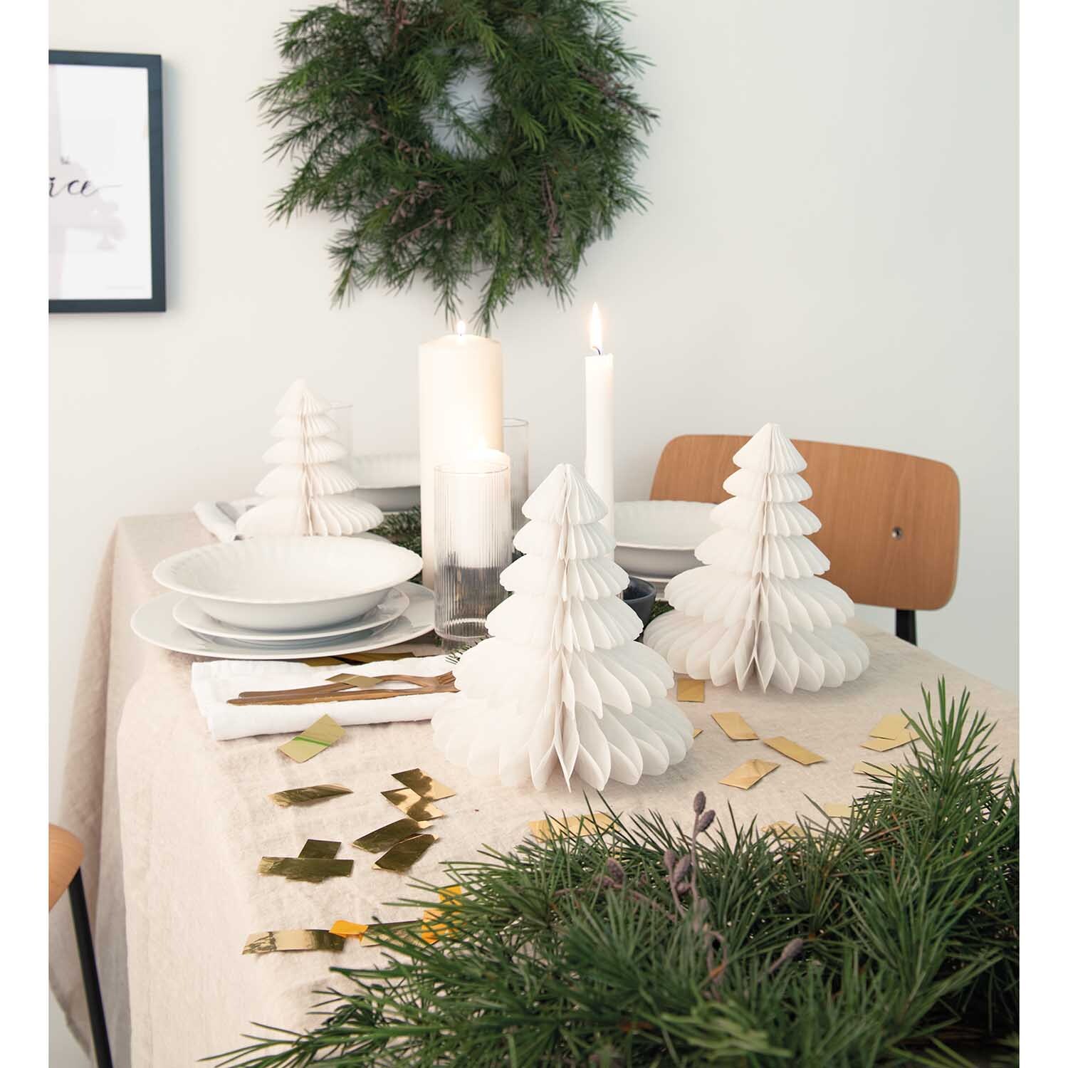 Wabenpapier Tannenbäume 20cm 3 Stück Farbe Weiß von Rico Design Wabenpapier Tannenbäume 20cm 3 Stück dekorieren einen festlichen Tisch in Weiß, umgeben von Kerzen und Tannenzweigen.