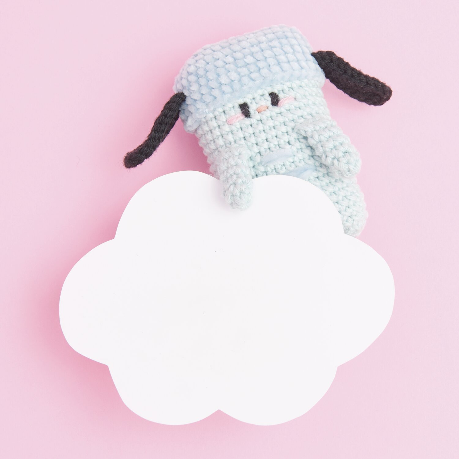 Ricorumi Rainbow Weirdos: Hellblaues Häkelspielzeug mit schwarzen Details auf rosa Hintergrund.