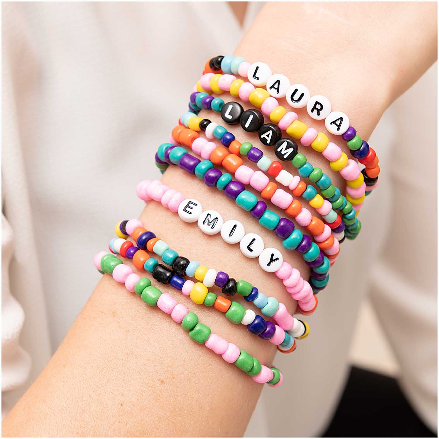 Keramik-Perlen natur multicolor 3mm 30g: Mehrfarbige Armbänder mit Buchstabenperlen an einem Handgelenk.