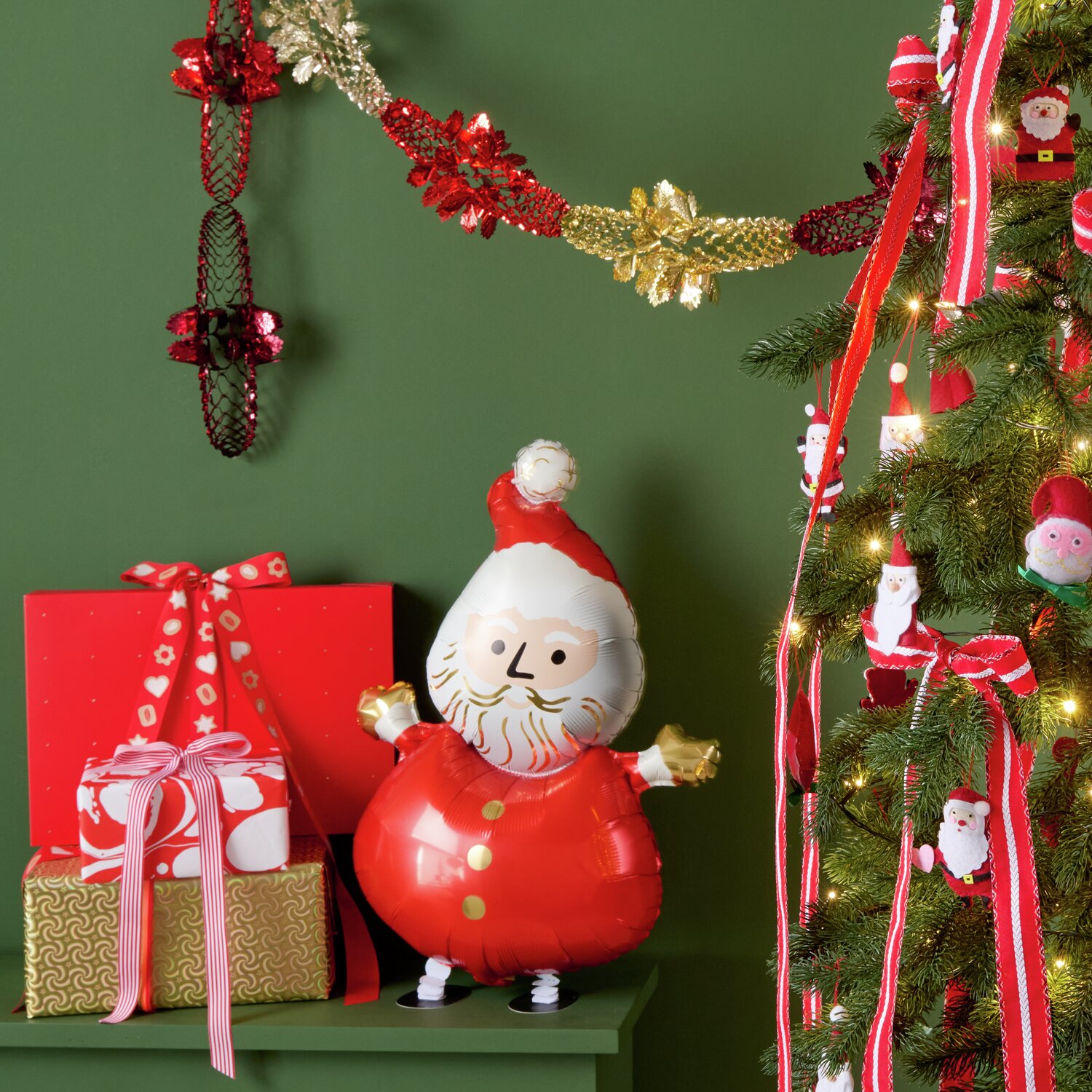 Folienballon Weihnachtsmann laufend neben geschmücktem Weihnachtsbaum und Geschenken.