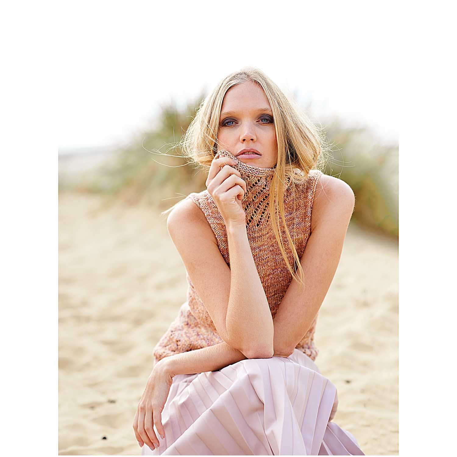 Creative Cotton Zickzack: Frau in gestricktem Oberteil am Strand, umgeben von Dünen, trägt Rico Design.