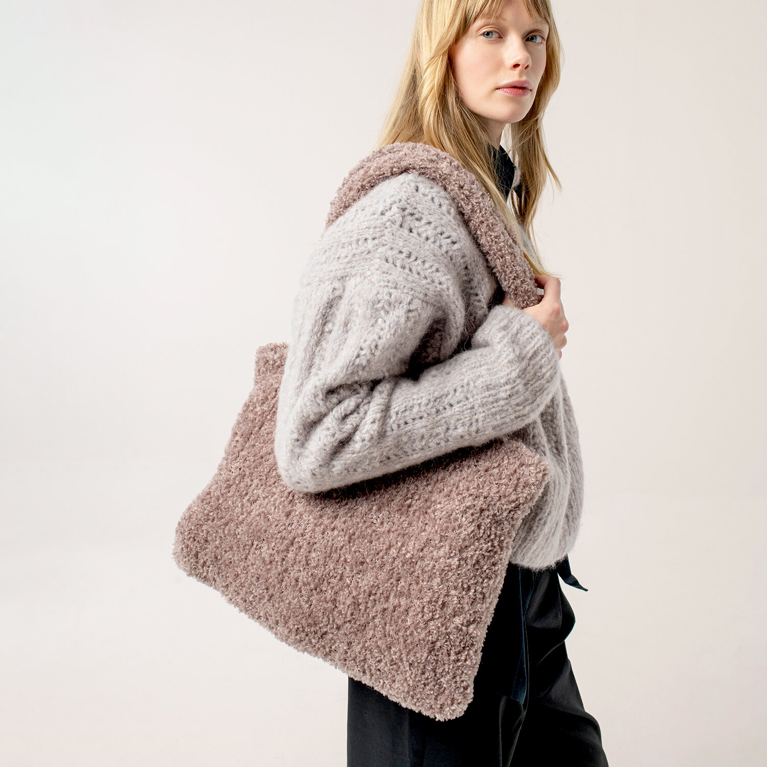 Strickanleitung Tasche aus Creative Teddy, große flauschige Schultertasche in Rosa-Beige, getragen von Frau im hellgrauen Strickpullover vor neutralem Hintergrund