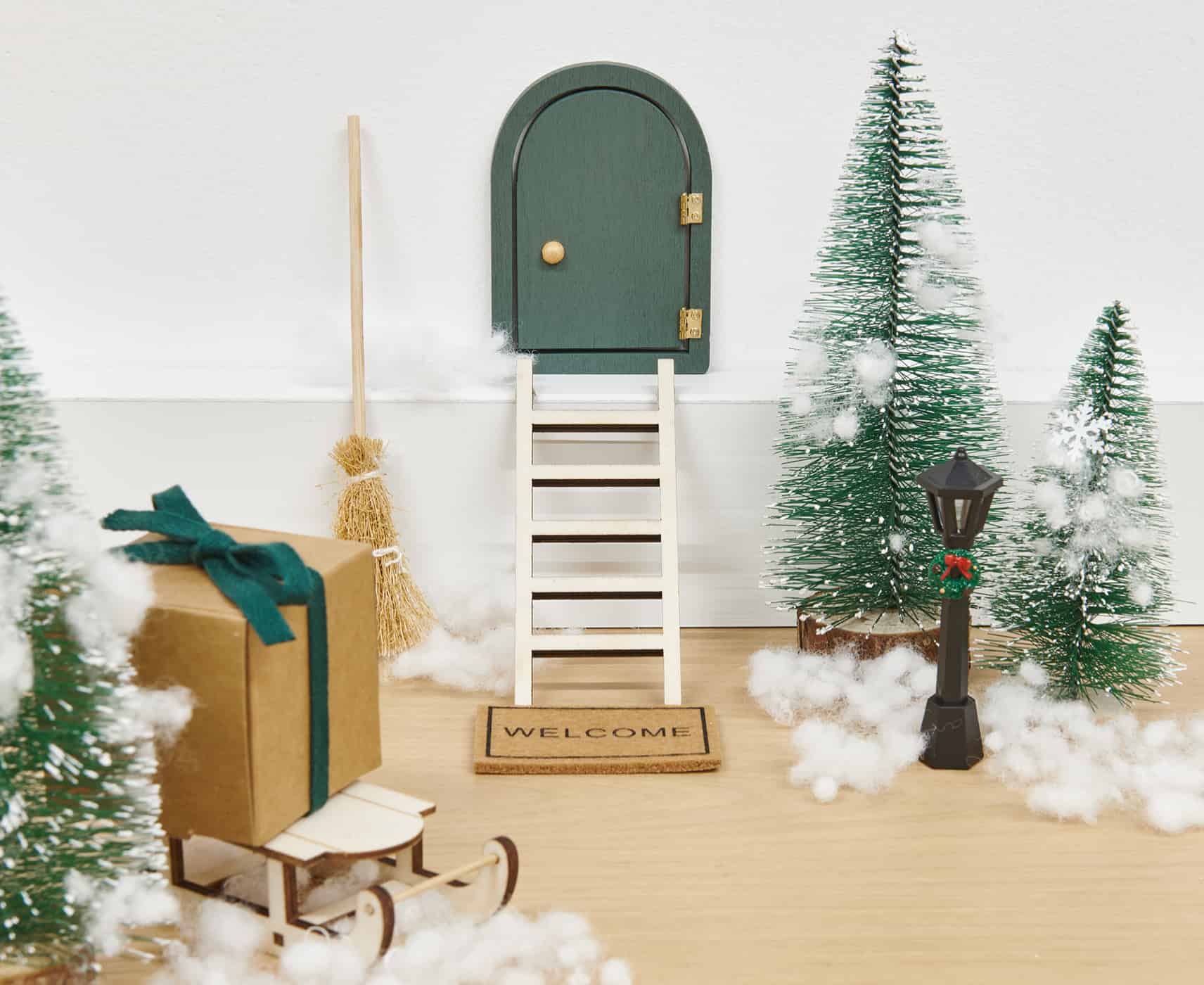 Miniatur Wichteltür ist dekoriert mit Tannenbäumen, Schnee aus Watte und Geschenken.