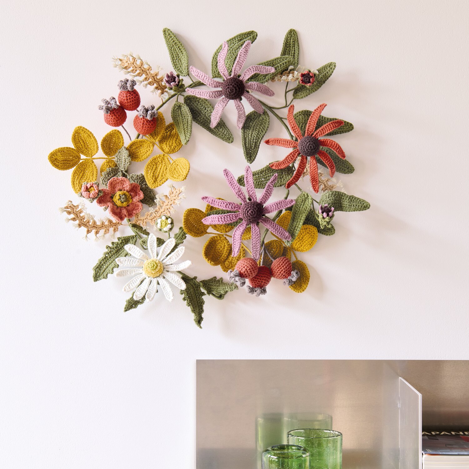 Ricorumi In the Meadow, dekorativer Häkelblumenkranz aus Creative Ricorumi dk in warmen Naturtönen an heller Wand, Subtitel 25g