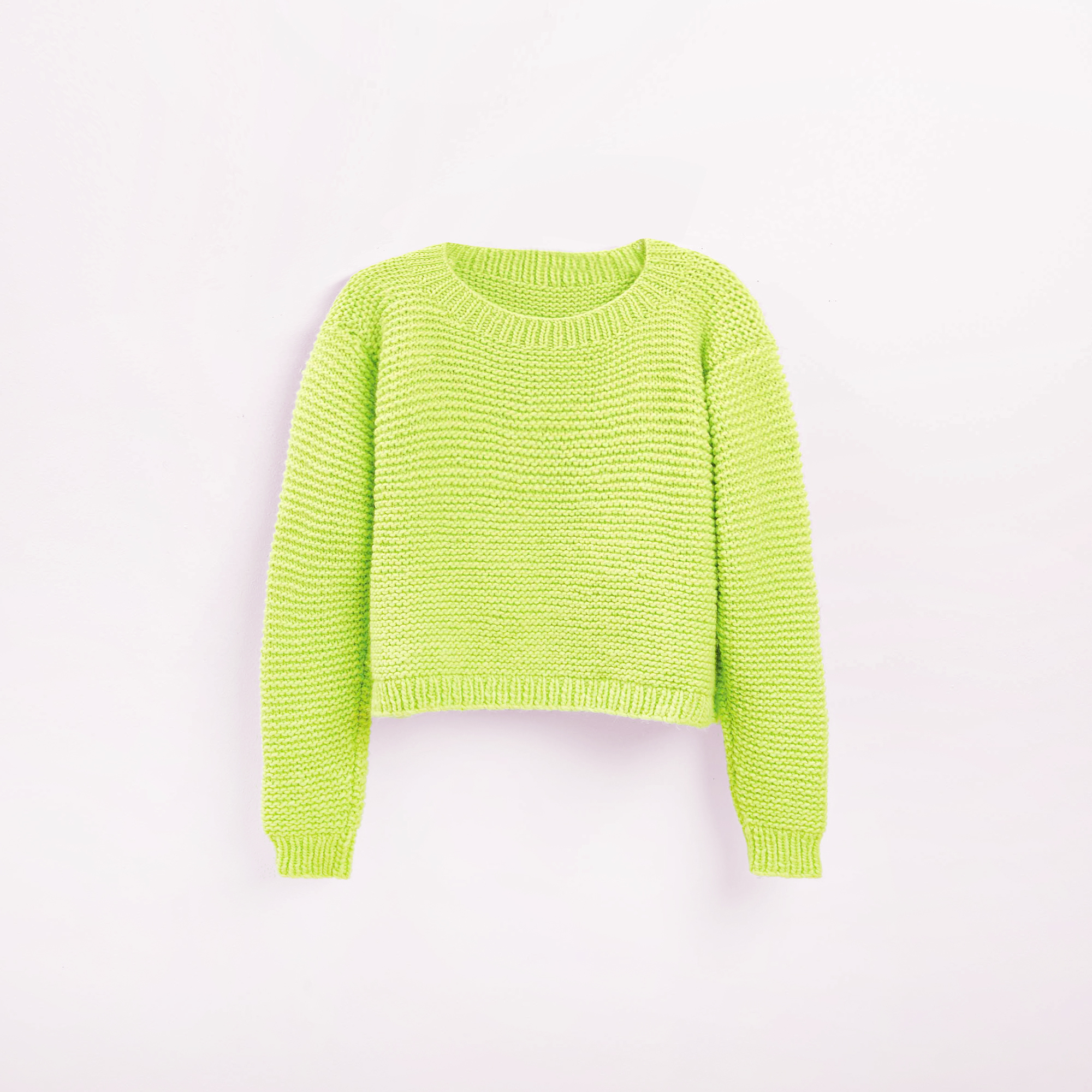 Gestrickter Pullover in Neongrün vor grauem Hintergrund